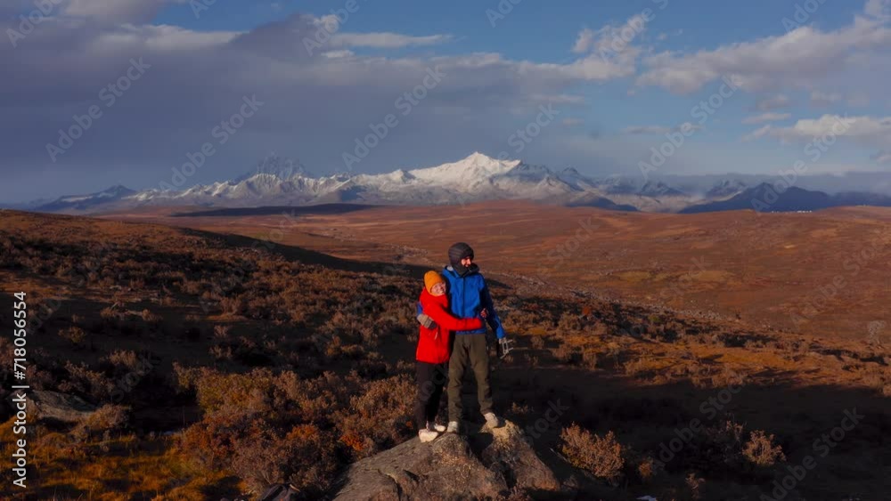 Young couple in warm clothes hugging each other with Gongga mount behind Young couple in warm clothes hugging each other with Gongga mount behind