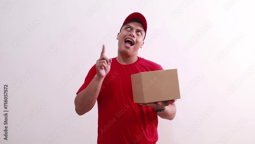 Young asian courier man holding packet on cardboard while pointing above. Isolated on white