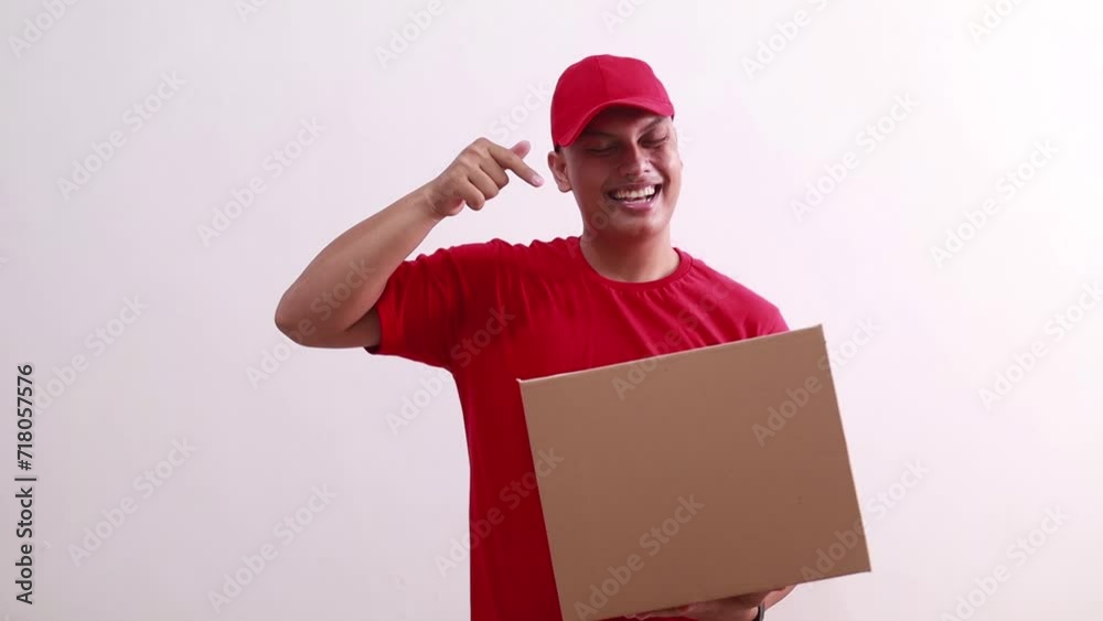 Happy young asian courier man holding cardboard while pointing on it. Isolated on white
