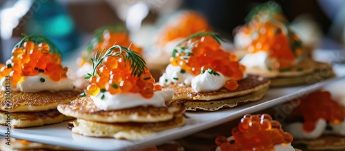 At the gourmet party, guests indulged in festive appetizers, savoring the delicate Mini Blini pancakes topped with creamy sour cream and decadent red caviar.