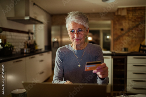 Senior woman holding credit card with laptop on desk at home photo