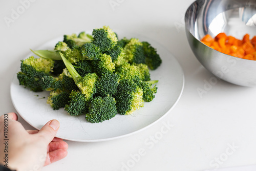 holding a plate of raw fresh broccoli against white table