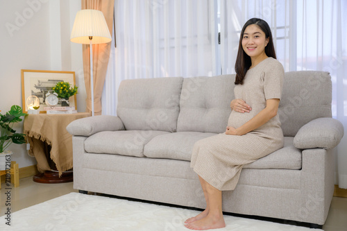 Picture of asian pregnant woman sitting on sofa in living room at home Carrying a large belly She smiles looking at the camera and is happy at her home