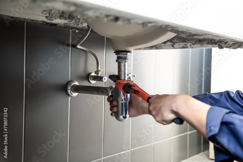 Plumber uses wrench to repair water pipe under sink There is maintenance to fix the water leak in the bathroom.with red wrench, plumbing install concept.