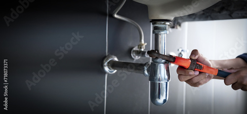 Plumber uses wrench to repair water pipe under sink There is maintenance to fix the water leak in the bathroom.with red wrench, plumbing install concept.