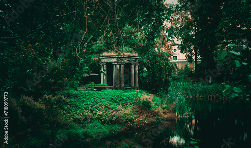 Fotografi In the overgrown green garden there is an old stone crypt on a summer evening