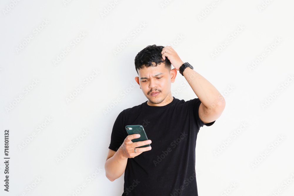 Portrait of unhappy Asian man in black shirt holding mobile phone with sad expression on face