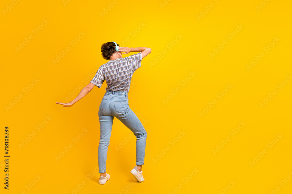 Full body rear behind photo of overjoyed nice lady hand touch headphones dancing empty space isolated on yellow color background