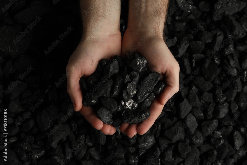 Man holding coal in hands over pile, top view