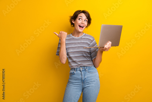 Photo of astonished impressed woman dressed t-shirt hold laptop directing at big discount empty space isolated on yellow color background