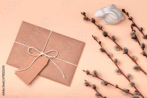 Craft envelope and blank label on a peach background with willow branches and Easter bunny. Easter greeting card.