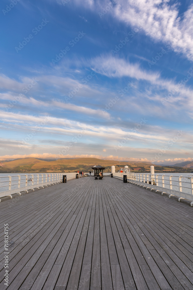 Wispy high clouds over a long wooden pier with mountains in the distance. Beaumaris Pier in North Wales