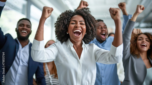 Joyful office workers are celebrating a success with their hands raised in the air and big smiles on their faces in a bright, modern office space.