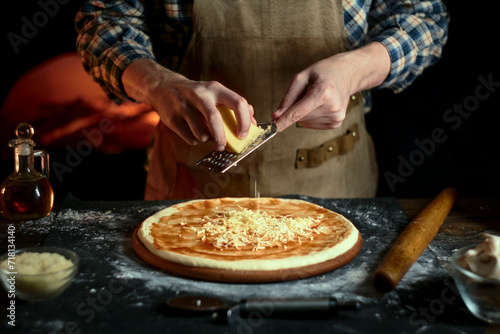 Chef grates cheese on pizza. A guy in a leather apron is preparing pizza. Pizzaiolo at work.