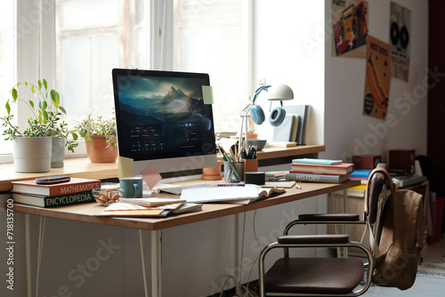 Workplace of solopreneur, student or designer with computer monitor, books, notepads ang group of flowerpots standing along windowsill © pressmaster