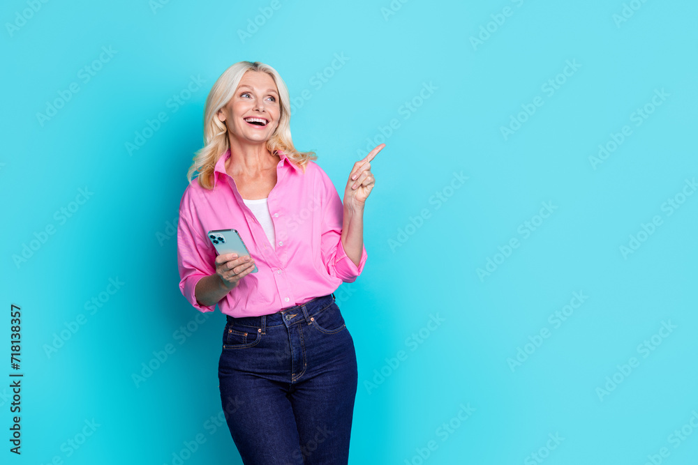 Photo portrait of lovely senior lady hold gadget point empty space wear trendy smart casual garment isolated on cyan color background Photo portrait of lovely senior lady hold gadget point empty space wear trendy smart casual garment isolated on cyan color background