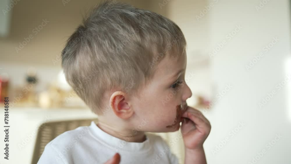 Child children eat sweet chocolate at table. Dirty face child mouth biting cocoa chocolate with teeth. Sweet breakfast of children at the table in kitchen. Happy kids with messy face eating chocolate Child children eat sweet chocolate at table. Dirty face child mouth biting cocoa chocolate with teeth. Sweet breakfast of children at the table in kitchen. Happy kids with messy face eating chocolate