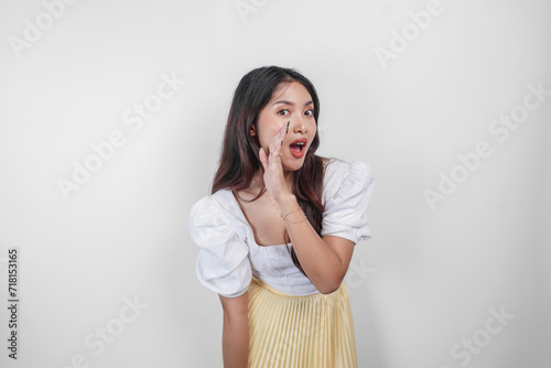 A young beautiful Asian woman is shouting and screaming loud with a hand on her mouth, isolated by white background.