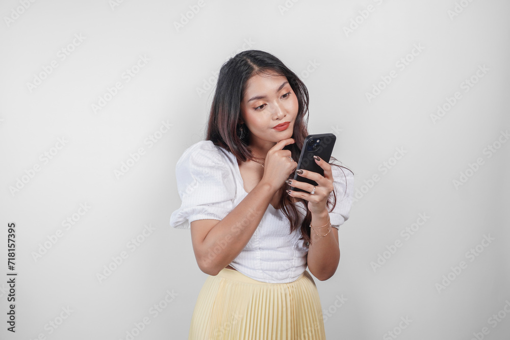 A thoughtful Asian woman is holding her smartphone while imagining her thoughts, isolated by white background.