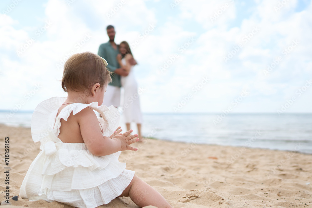 A photoshoot of happy parents admiring their 1 year old girl playing with sand on the beach