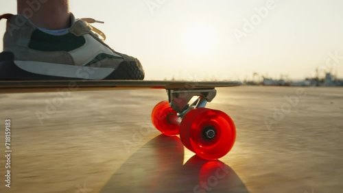 Sporty skater male riding longboard with red wheels shod in sneakers with high socks bottom view against backdrop of seaport at sunset in summer on vacation. Travel. Lifestyle freedom photo