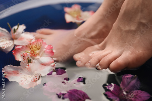 Woman soaking her feet in bowl with water and flowers, closeup. Spa treatment