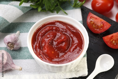 Organic ketchup in bowl, fresh tomatoes and garlic on table, closeup. Tomato sauce