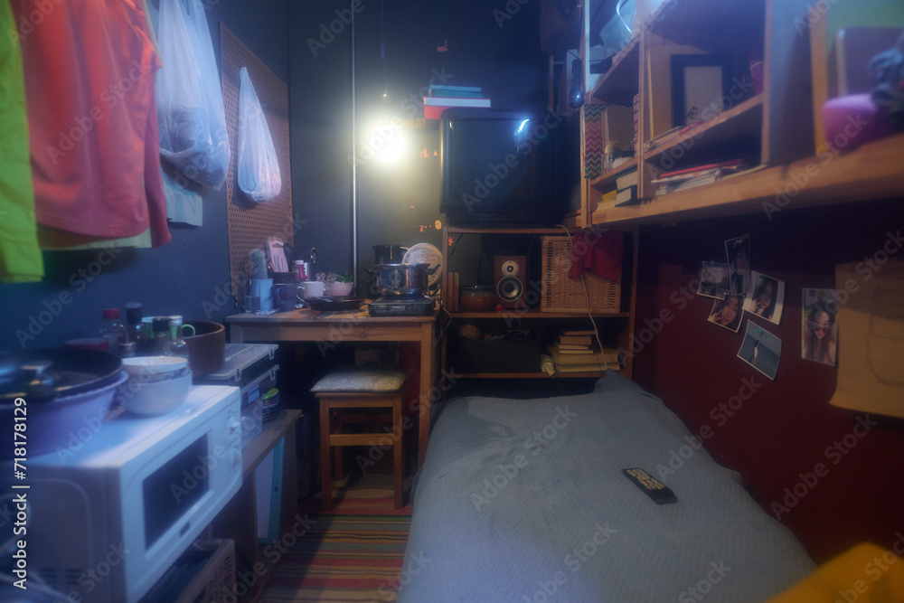 Small apartment with wooden kitchen table standing next to shelf with old TV set and other stuff in front of single bed and household appliances Small apartment with wooden kitchen table standing next to shelf with old TV set and other stuff in front of single bed and household appliances