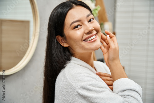 portrait of happy young asian with acne-prone skin standing in modern bathroom and looking at camera photo