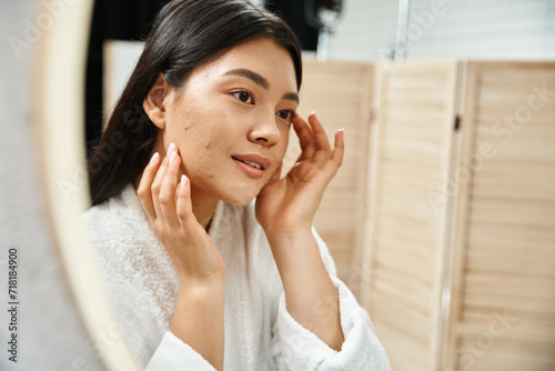 young asian woman with brunette hair examining her skin in the bathroom mirror, skin condition photo