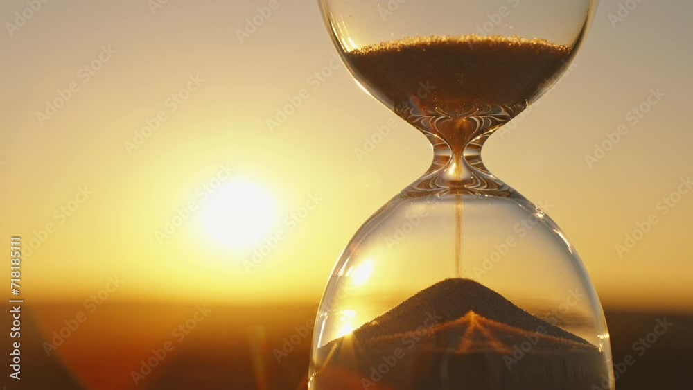 Hourglass concept on blurred background of golden sun disk sky in sunset rays in summer closeup. Golden sand pours quickly. Time concept sand. Relax