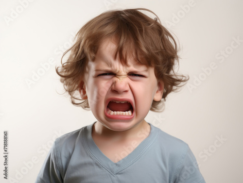 Close-up of a young child crying intensely, showing signs of frustration and anger against a plain background. © Anna