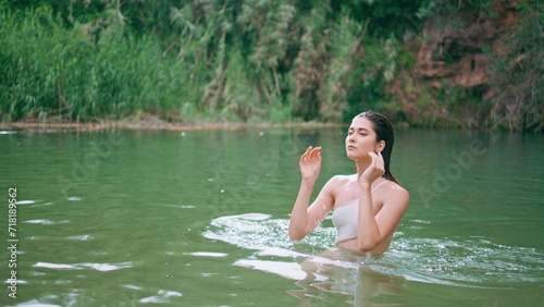 Wet lady emerging pond looking camera portrait. Model touching hair at lake aqua