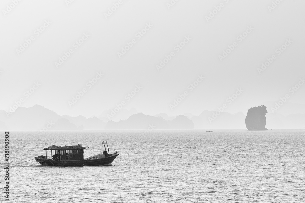 Fishing boat on a foggy day in Ha Long Bay with rock formation on the right