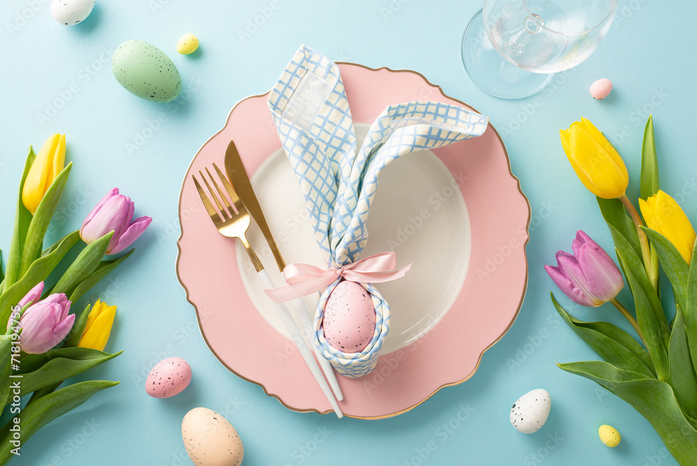 Bunny-themed Delight: Top-down view of an enchanting Easter table setting with bunny ear napkin, plate, cutlery, wine glass, tulips, and colorful eggs. Pastel blue background
