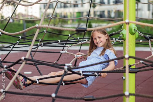 Smiling child girl lying on rope net playground.
