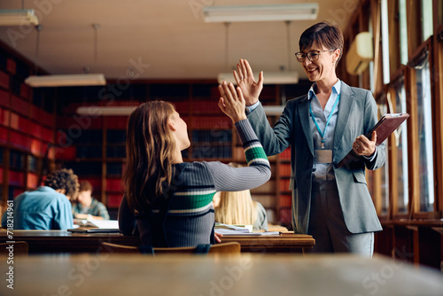 Happy high school teacher and her student giving high five in classroom.