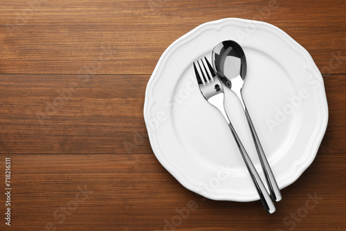 Clean plate  spoon and fork on wooden table  top view. Space for text