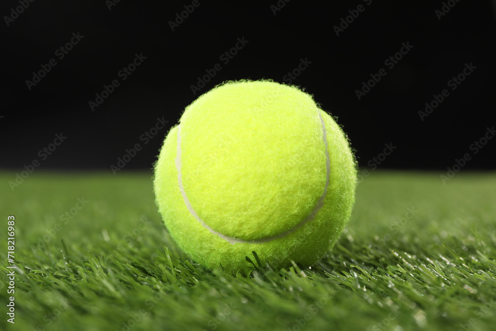 Tennis ball on green grass against black background, closeup