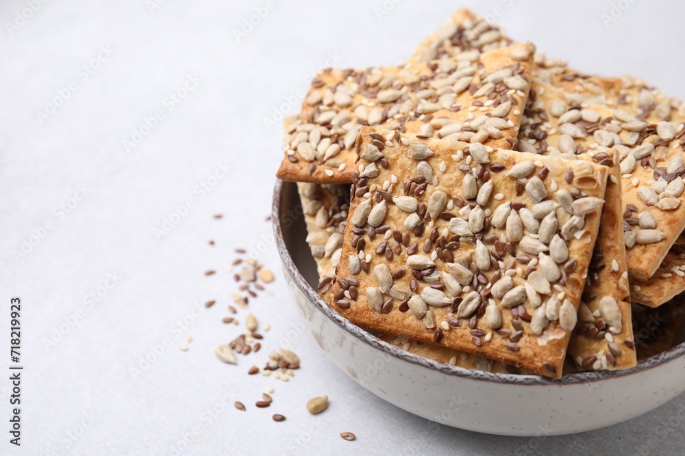 Cereal crackers with flax, sunflower and sesame seeds in bowl on light textured table, closeup. Space for text Cereal crackers with flax, sunflower and sesame seeds in bowl on light textured table, closeup. Space for text