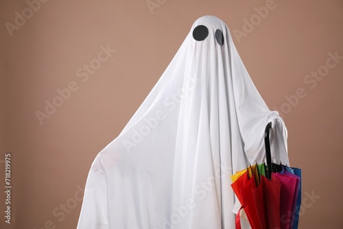 Person in ghost costume with rainbow umbrella on dark beige background, space for text