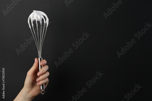 Woman holding whisk with whipped cream on black background, closeup. Space for text photo