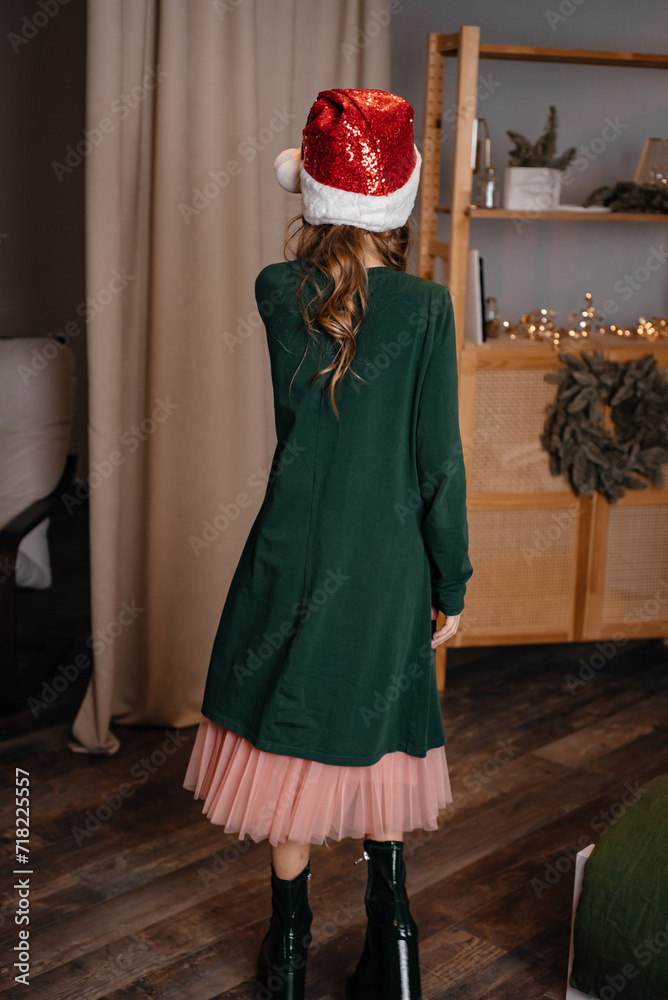 A little girl 9 years old in a New Year's santa hat plays on New Year's Eve. Portrait of a child in the holiday of Christmas.