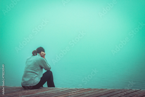 Junge Frau sitzt einsam am Rand eines Holzweges einer Brücke gebückt. photo