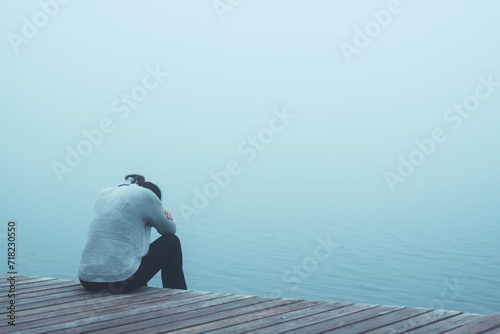 Junge Frau sitzt einsam am Rand eines Weges gebückt und traurig mit dem Kopf in den Armen versteckt Rückansicht photo