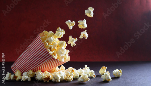 Delicious popcorn scattering from a red striped carton box on a dark red background