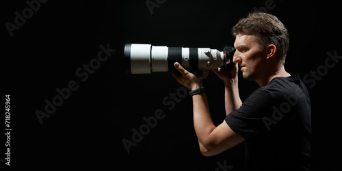 young photograph aiming with camera and big white lens isolated on black background