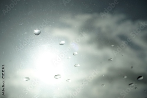 Abstraktes Motiv mit Regentropfenmuster vor grauem Himmel mit weißem Sonnenlicht bei Regen und Sonne am Morgen im Winter