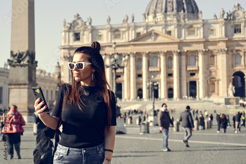Rome,Italy, Vatican City, Rome, Saint Peter's Basilica in St. Peter's Square Young beautiful woman using a mobile phone taking a pictures.Concept of Italian gastronomy and travel