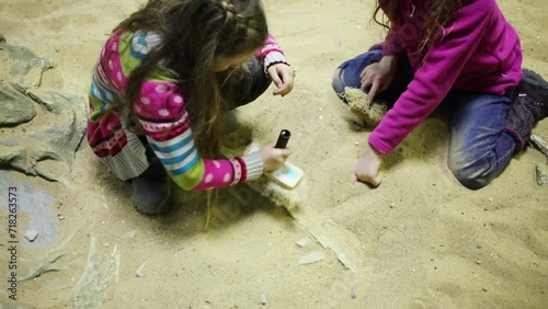 Two girls dig together in dry sand bones of dinosaurs photo